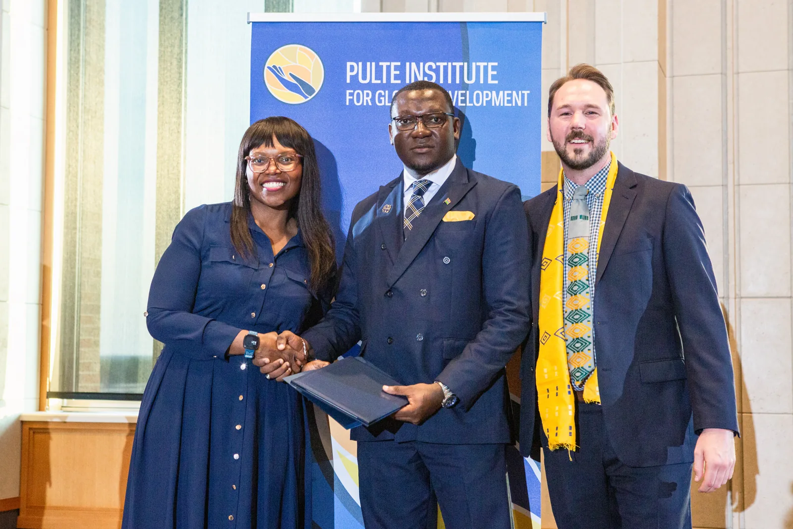 Three participants in formal attire beside a banner